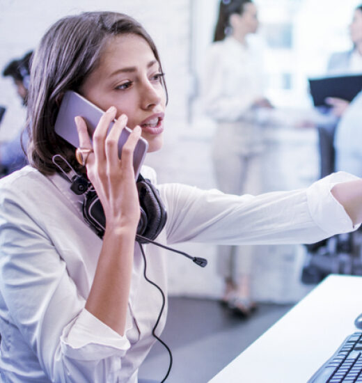 A young woman with a cell phone on her right ear and a headset around her neck being in a call.